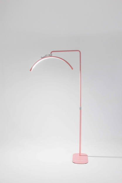 A pink floor lamp with a flexible neck, standing in a relaxed S shape, with a sturdy base. It has a switch on the stem and is connected to a power cord.